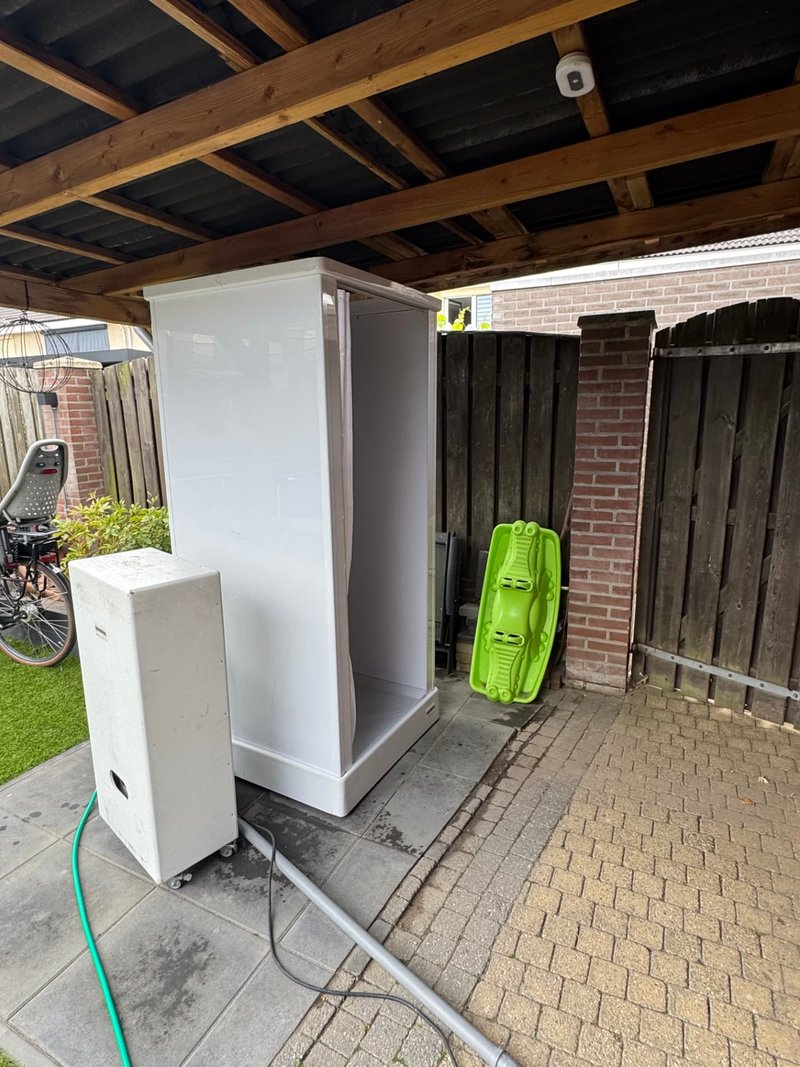 Mobiele buitendouche onder overkapping met boiler bij badkamerlekkage